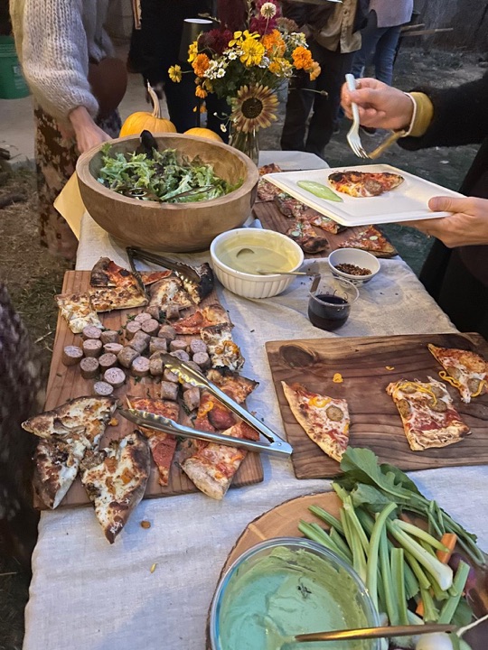 The dinner table: boards of wood-fired pizza and sausage, a big salad and dips.