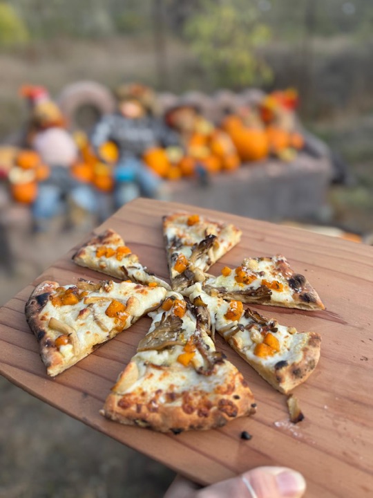 Slices of wood-fired pizza with squash and mushrooms on a board, straight from the oven.